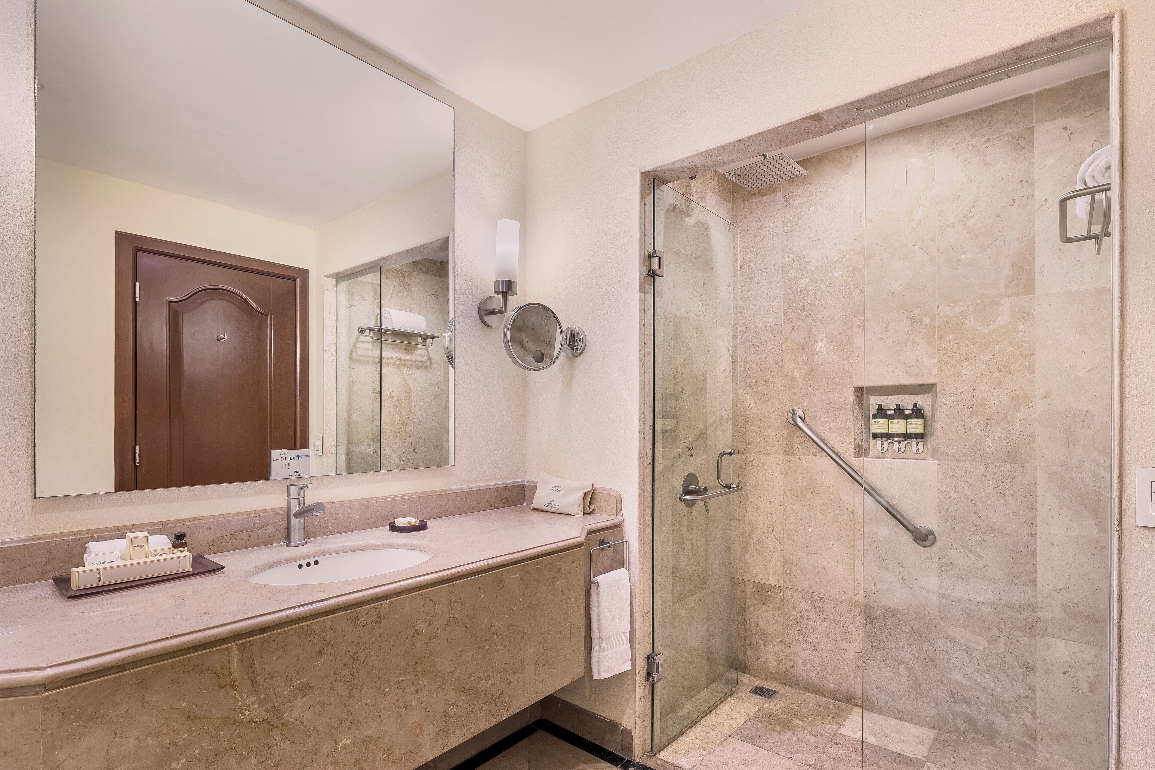 A bathroom with a large mirror, a sink, a shower with a glass door, and a towel rack.