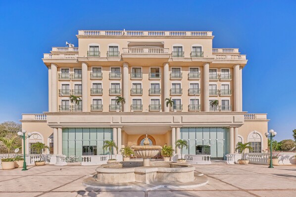 Un hotel grande de varios pisos con una fuente central, ventanas amplias y balcones.
