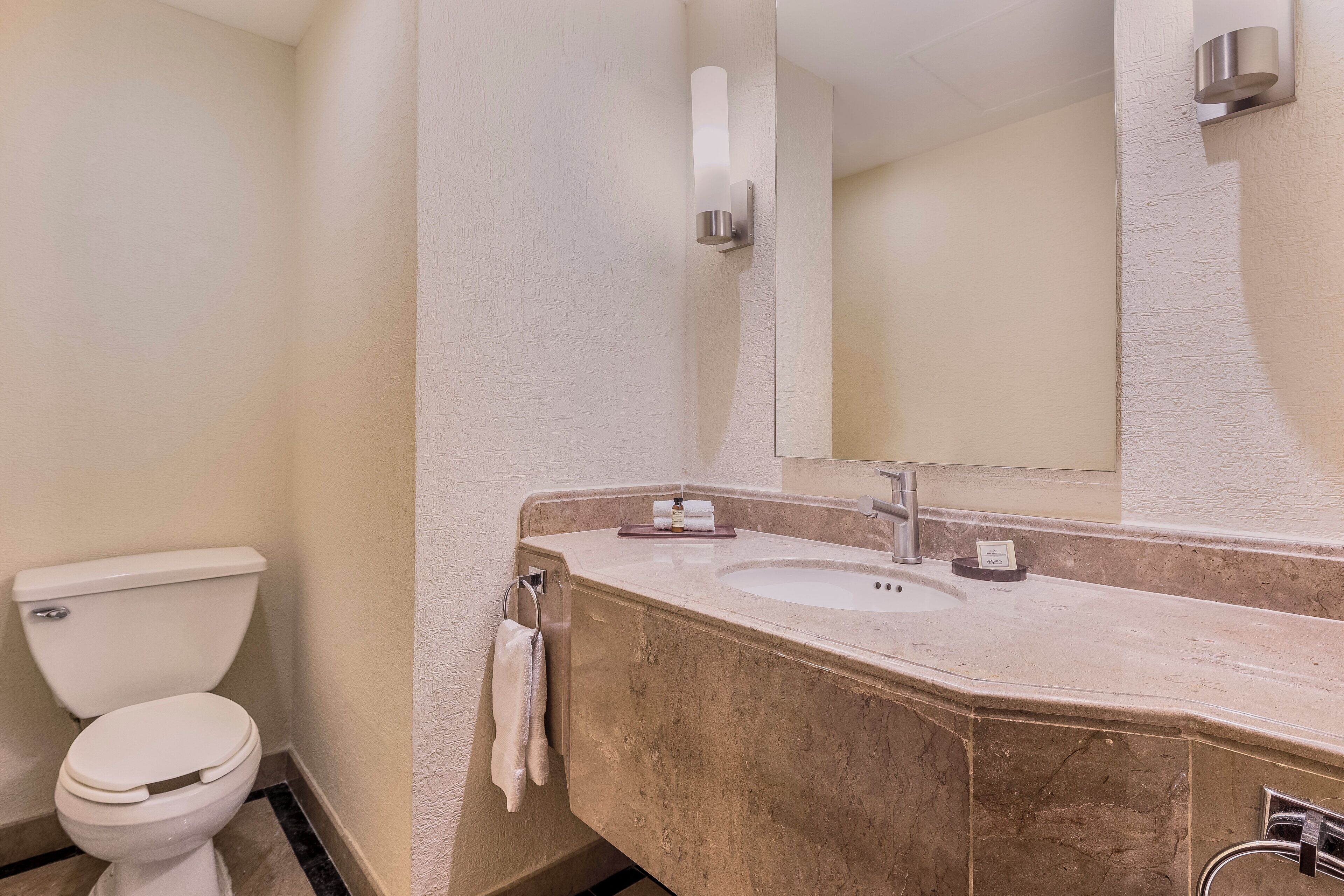 A bathroom with a toilet, sink, mirror, and towel rack.