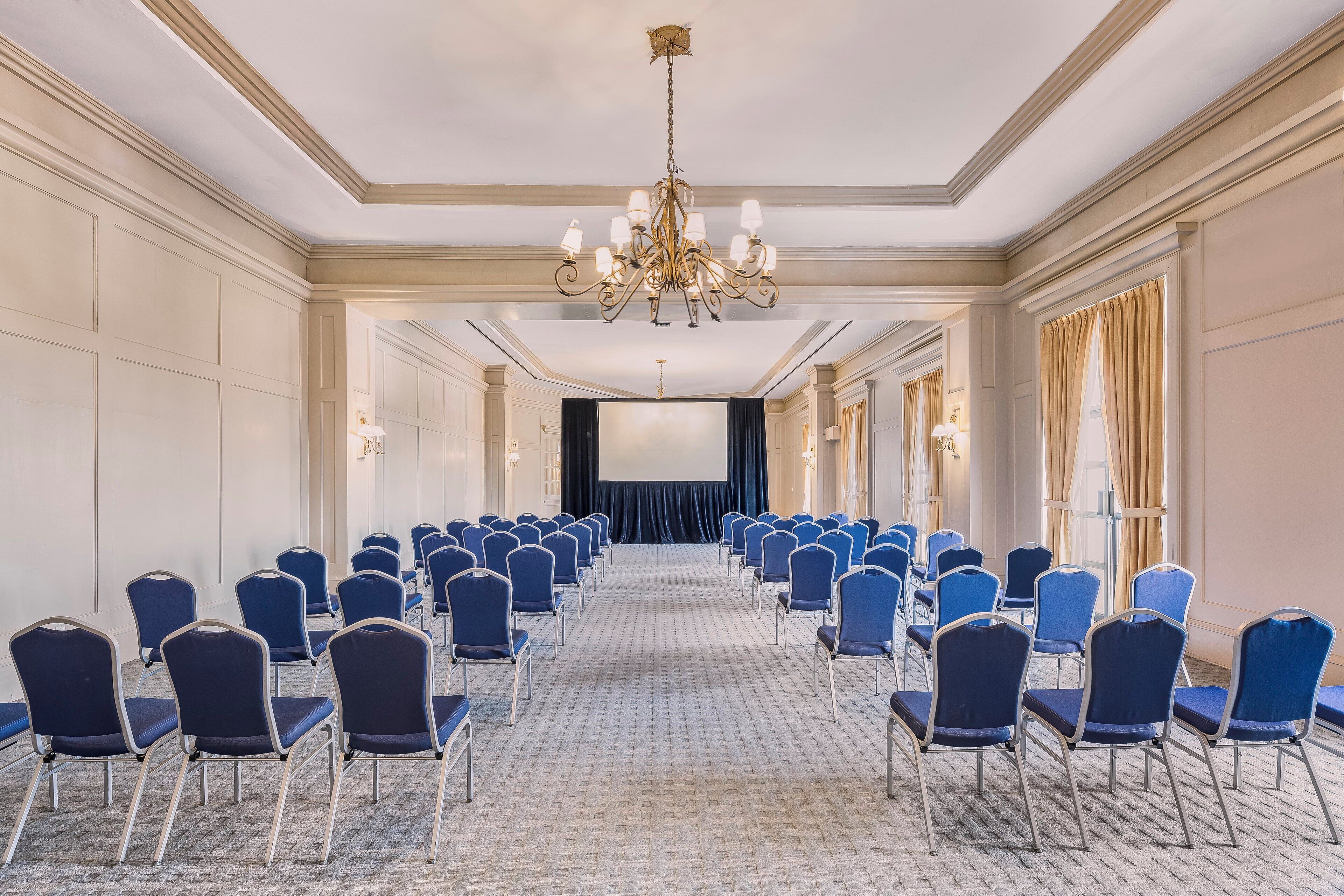 Un salón de conferencias con filas de sillas azules, una pantalla grande y una araña.