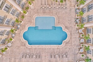 A rooftop pool with a rectangular shape, surrounded by lounge chairs and tables, and bordered by a low wall.