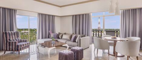 A spacious living room with a sofa, armchairs, ottomans, a coffee table, and a balcony with a view.