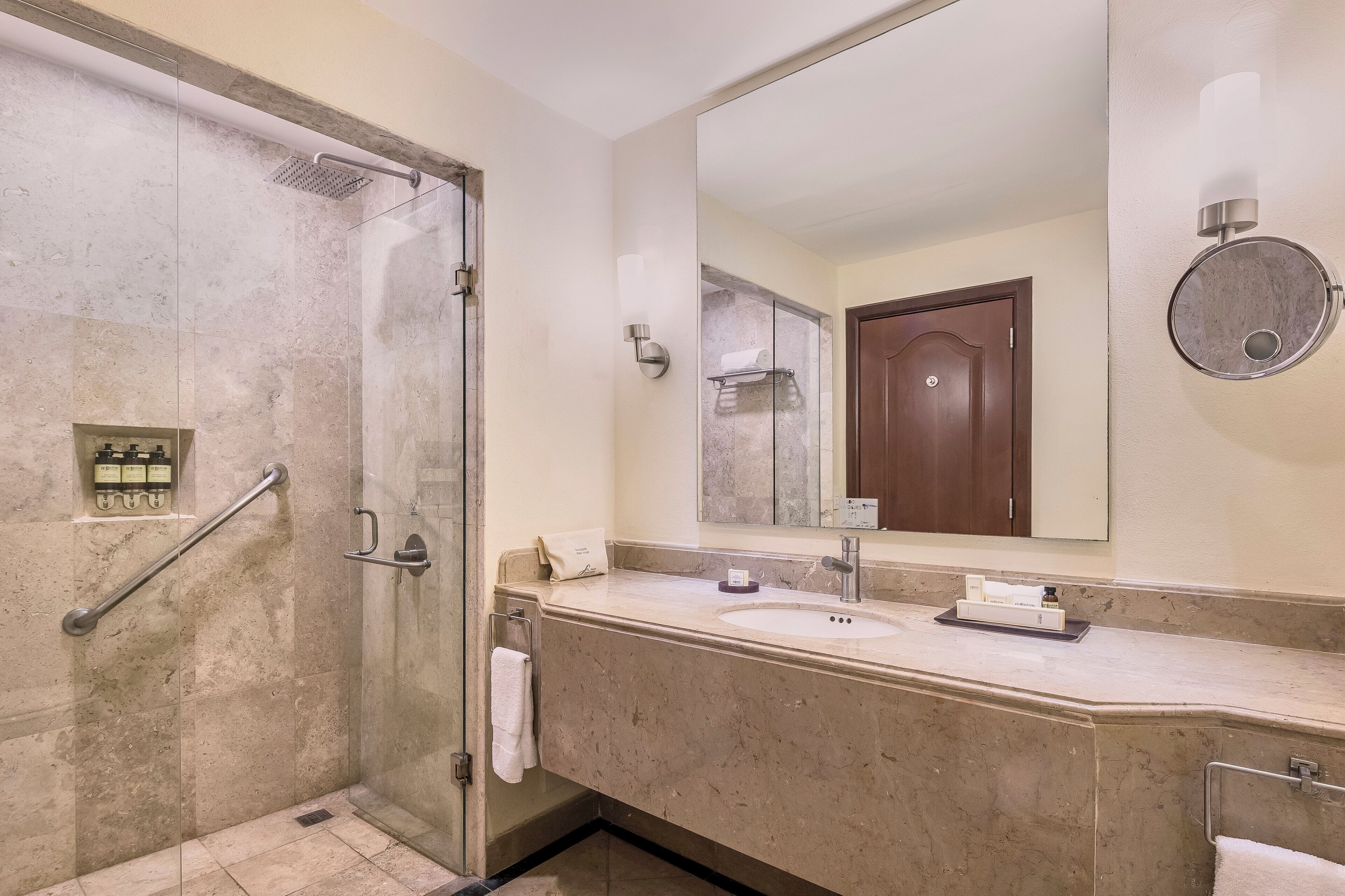 A bathroom with a glass-enclosed shower, a sink with a mirror above it, and a towel rack.