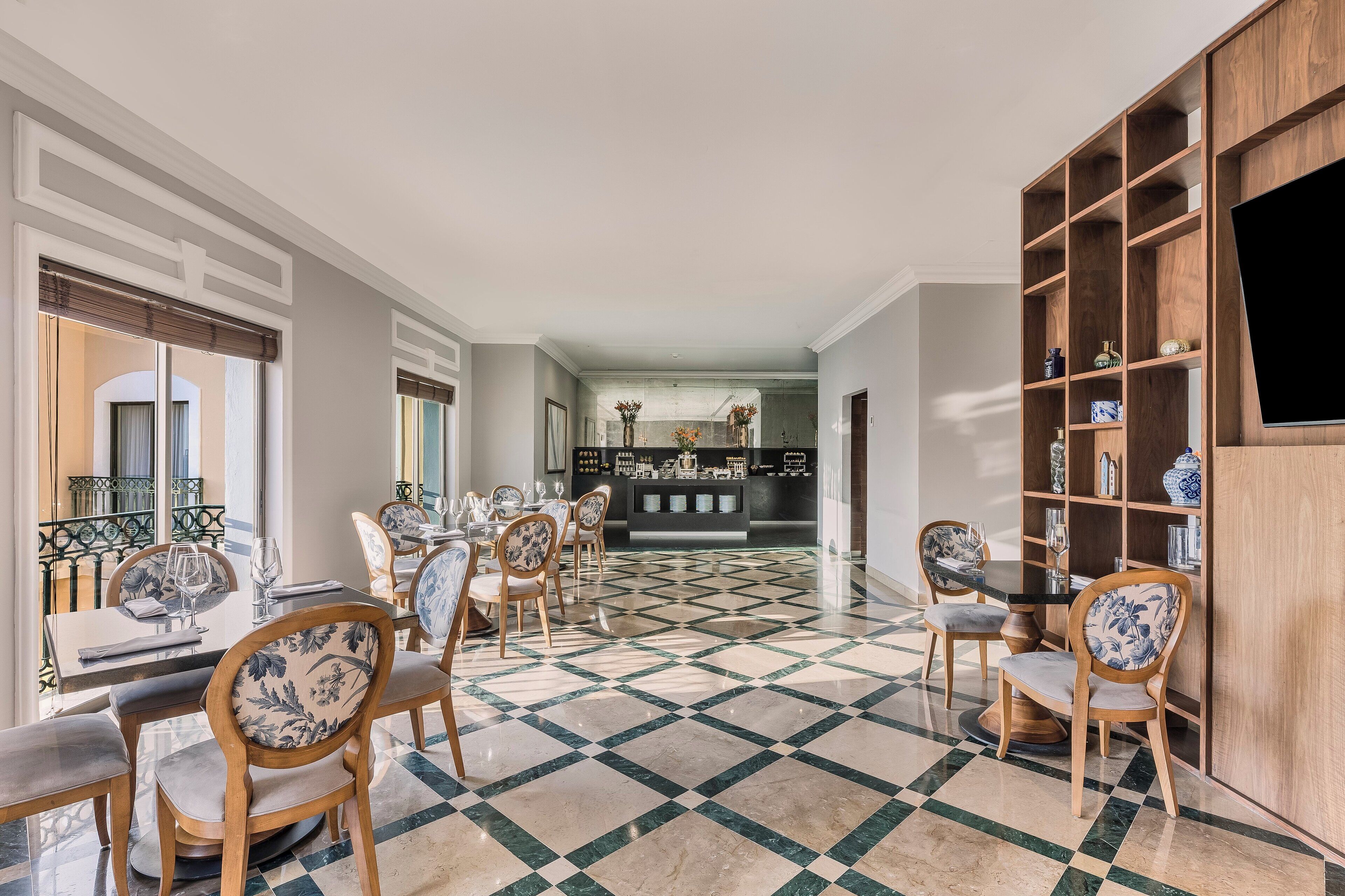 A dining area with a checkered floor, wooden chairs with floral upholstery, and a bar area in the background.