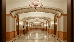 Um corredor amplo e bem iluminado, com piso de mármore polido, detalhado design no teto e elegantes lustres.