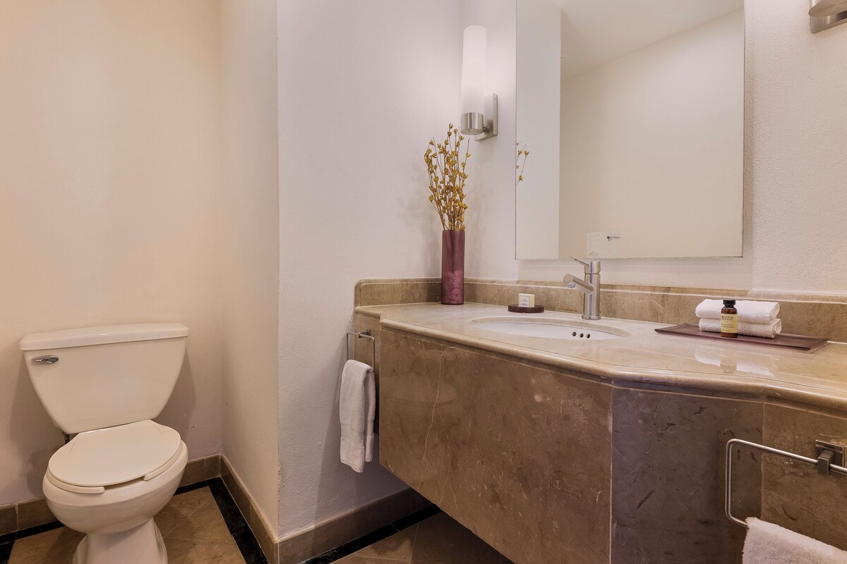 A bathroom with a toilet, a sink, a mirror, and a vase with dried flowers.