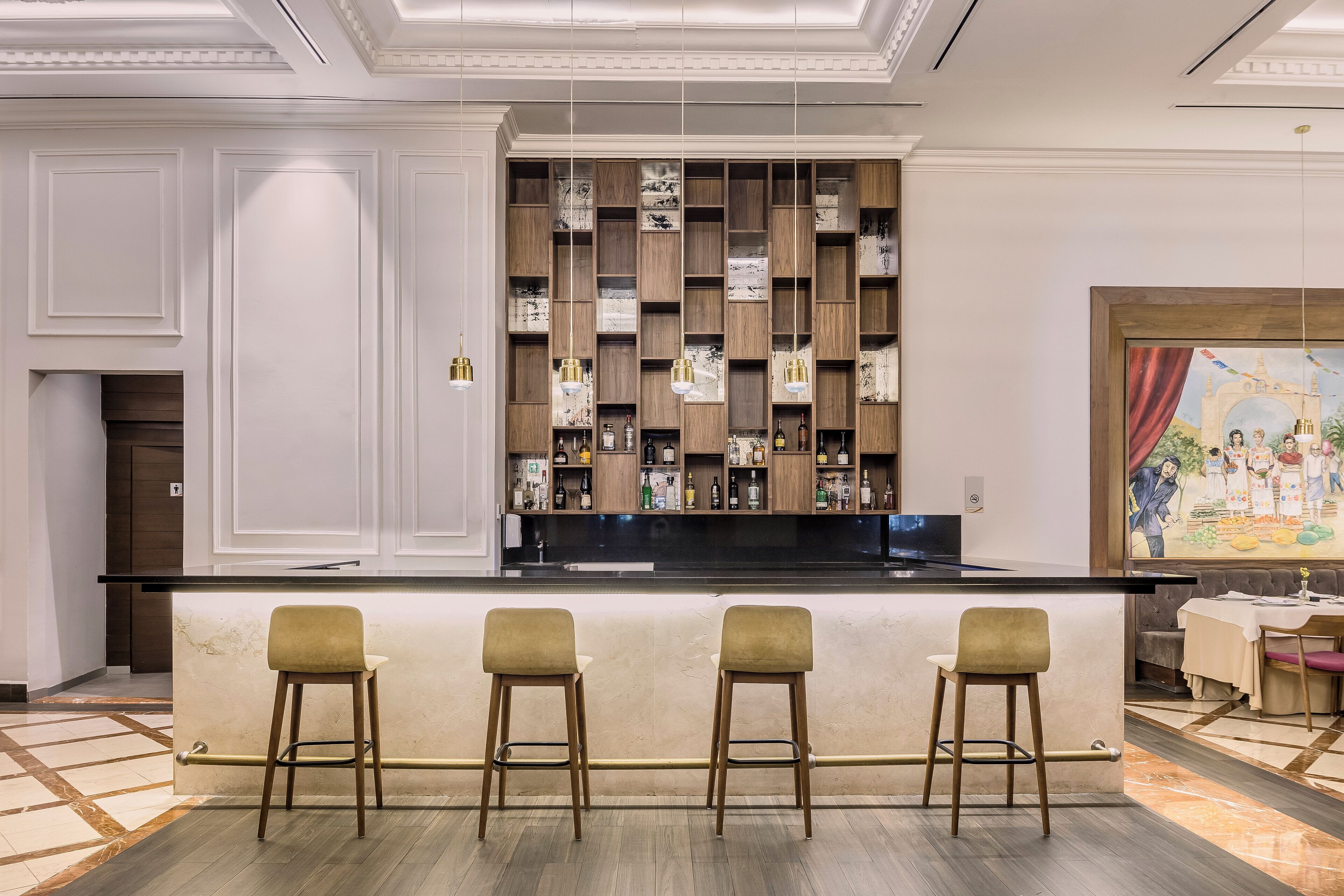 A bar area with a marble countertop, wooden shelves with bottles, and three bar stools.