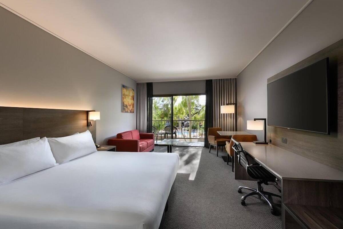 A hotel room with a large bed, a desk, a chair, a sofa, and a TV.
