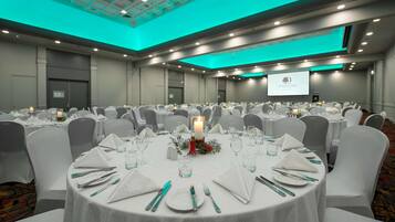 A large conference room with round tables, white chairs, and a central candle centerpiece.