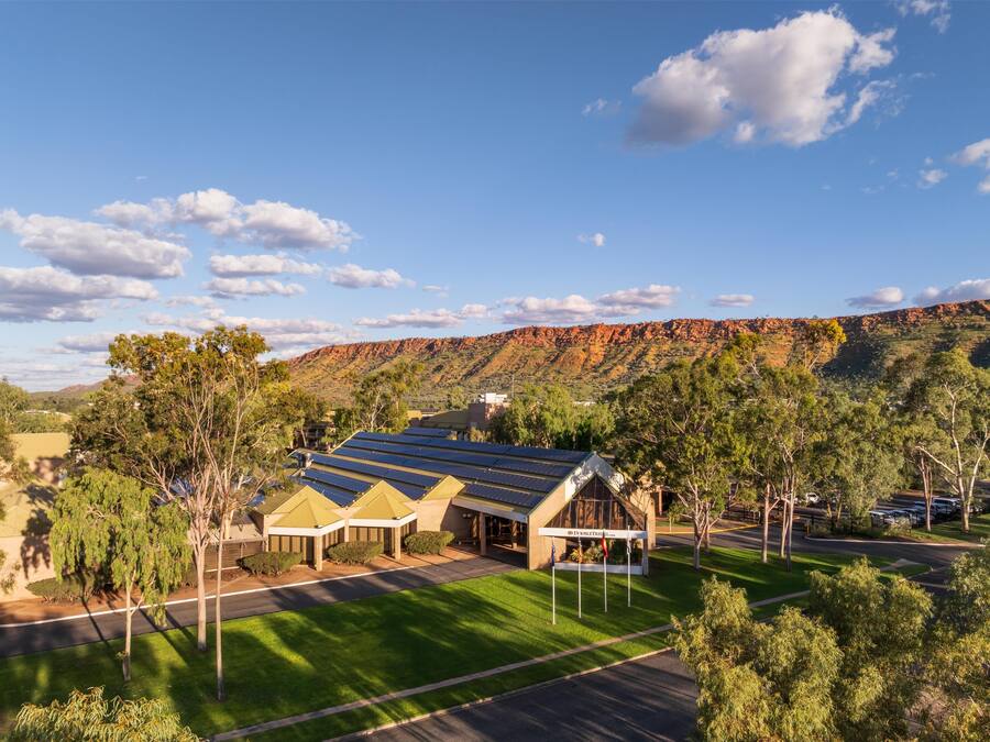 A building with solar panels, surrounded by trees and a hilly landscape.