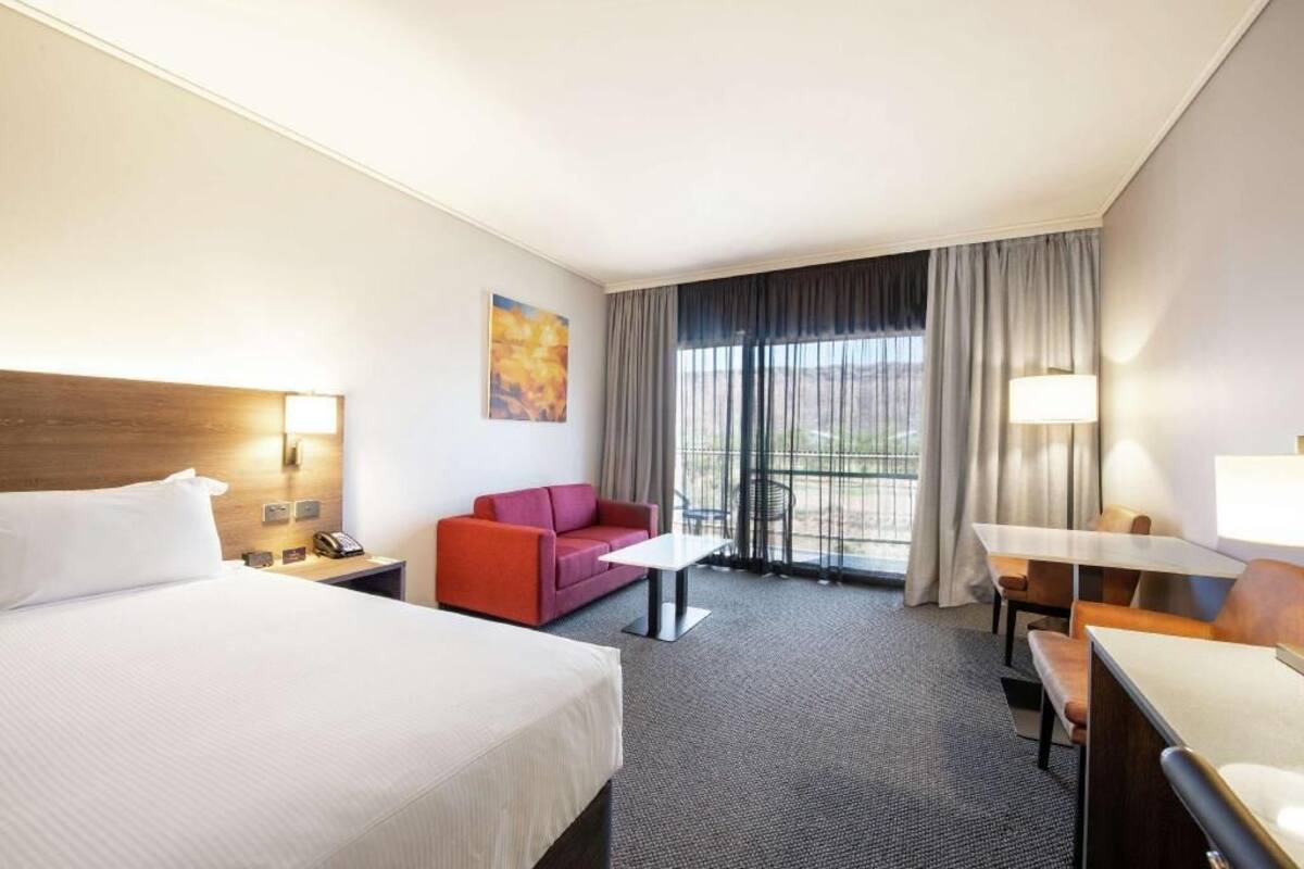 A hotel room with a bed, a desk, a chair, a sofa, and a window with curtains.