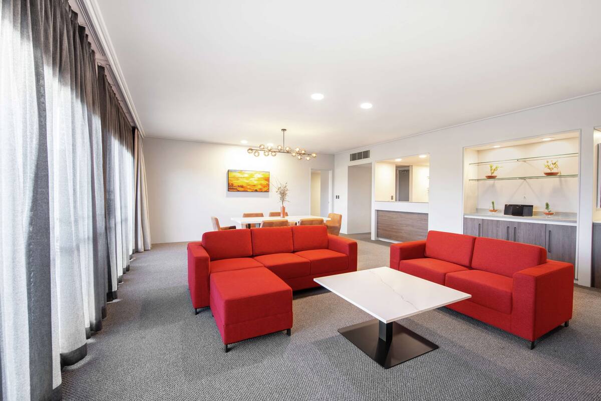 A modern hotel room with a sectional sofa, a dining area, a kitchen, and a living area.