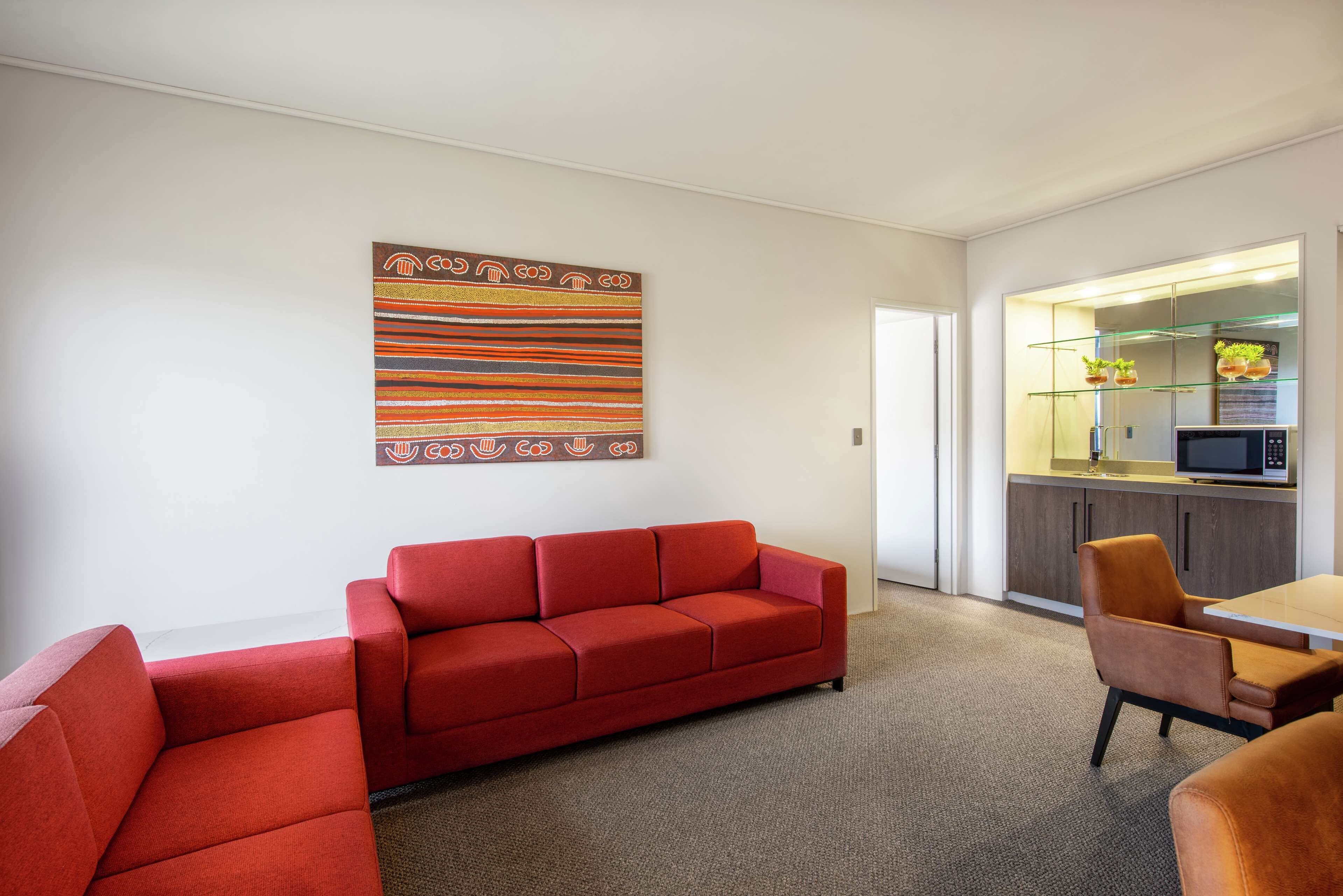 A modern living area with a red sofa, a dining table, and a kitchen area with a microwave.