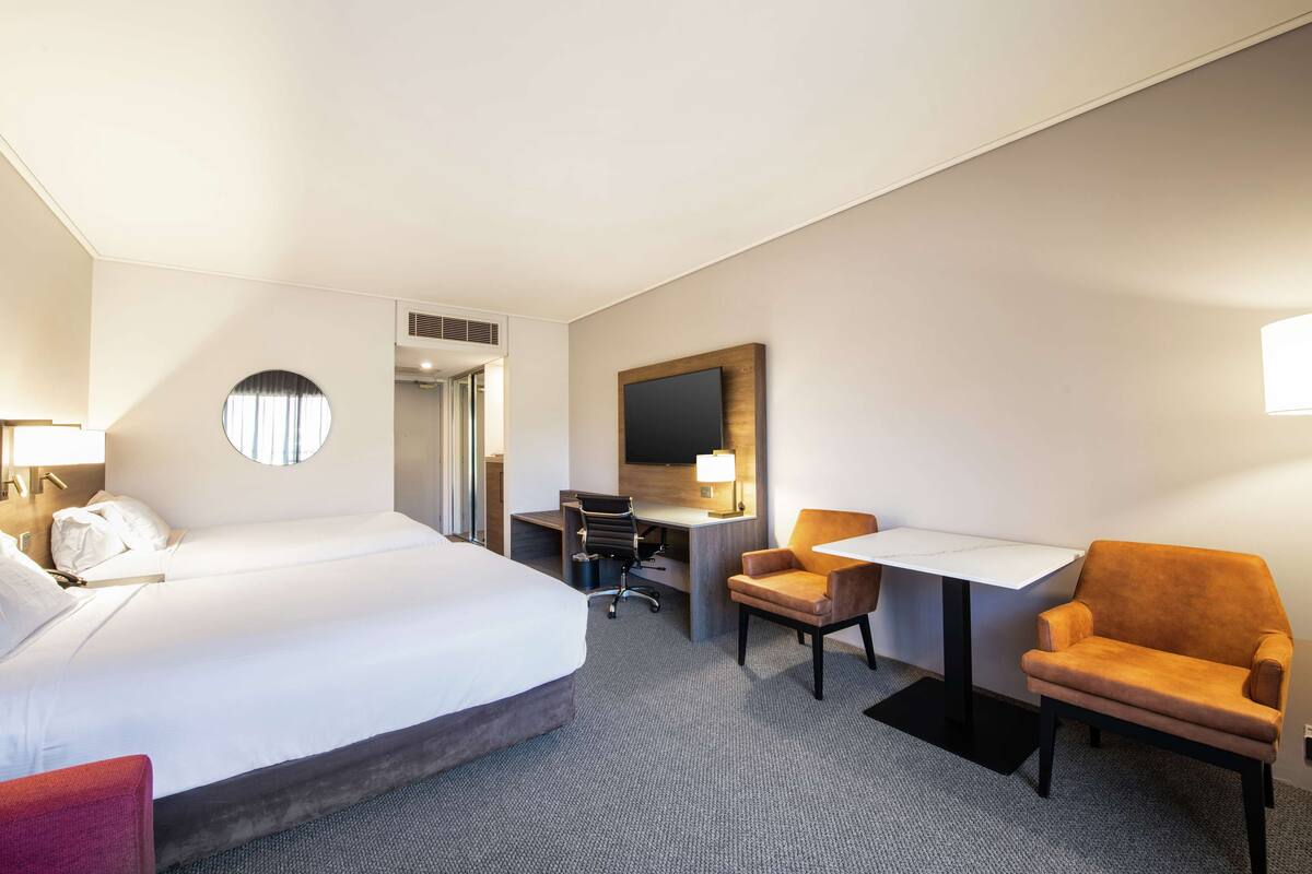 A hotel room with a large bed, a desk, a chair, and a small table.