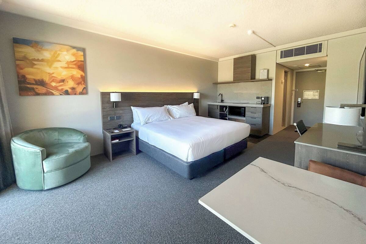 A hotel room with a bed, a desk, a chair, a nightstand, a lamp, and a painting on the wall.
