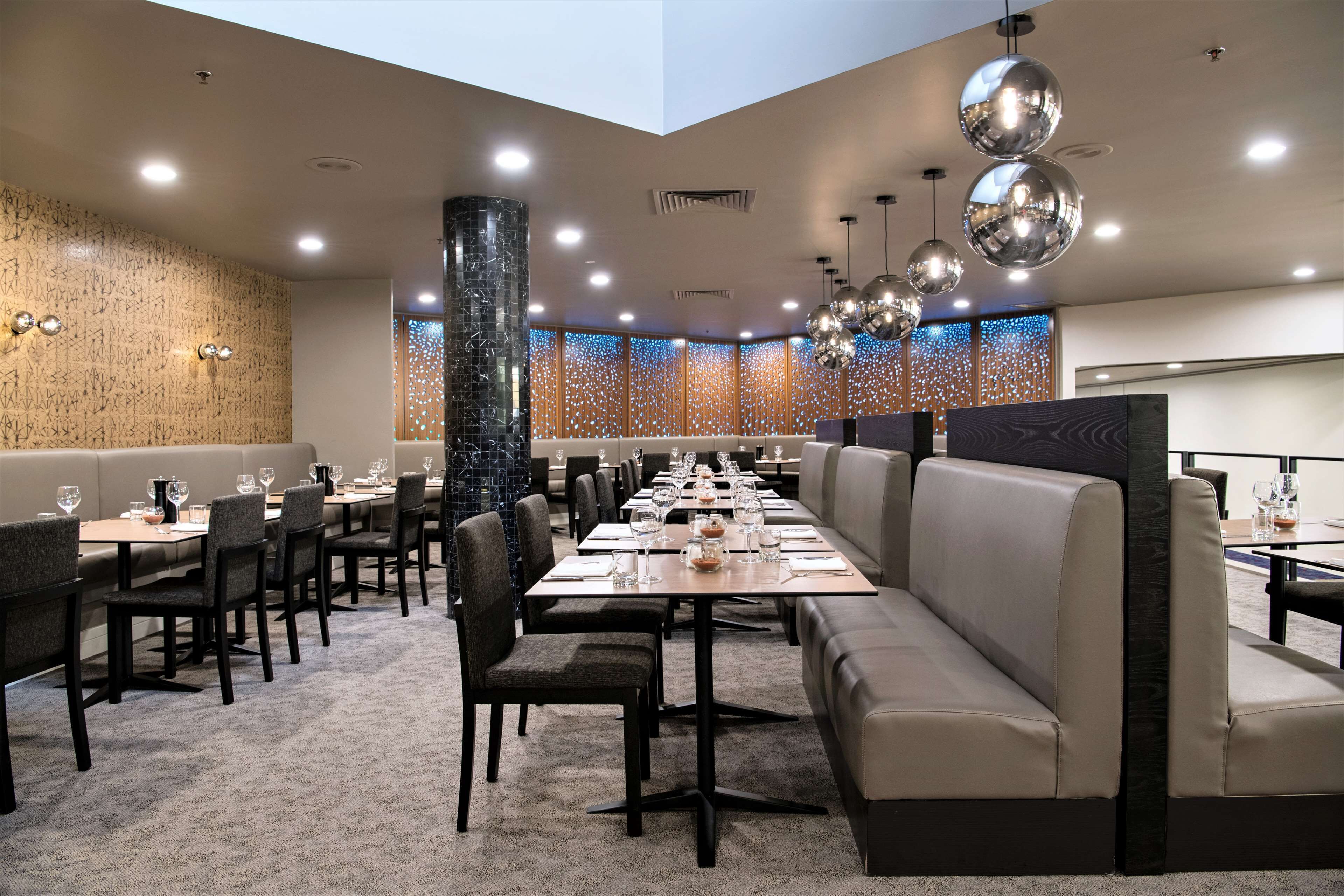 A modern dining area with long tables, cushioned seating, and decorative lighting.