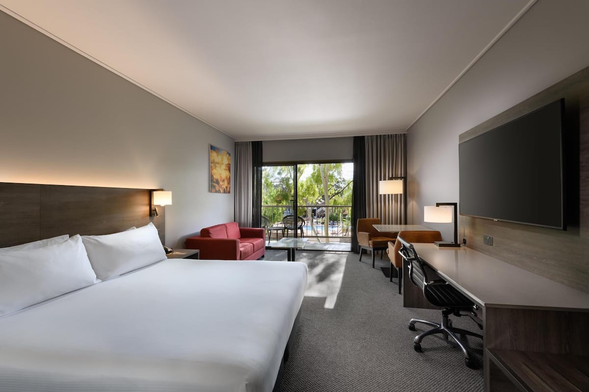 A hotel room with a large bed, a desk, a chair, a sofa, and a TV.