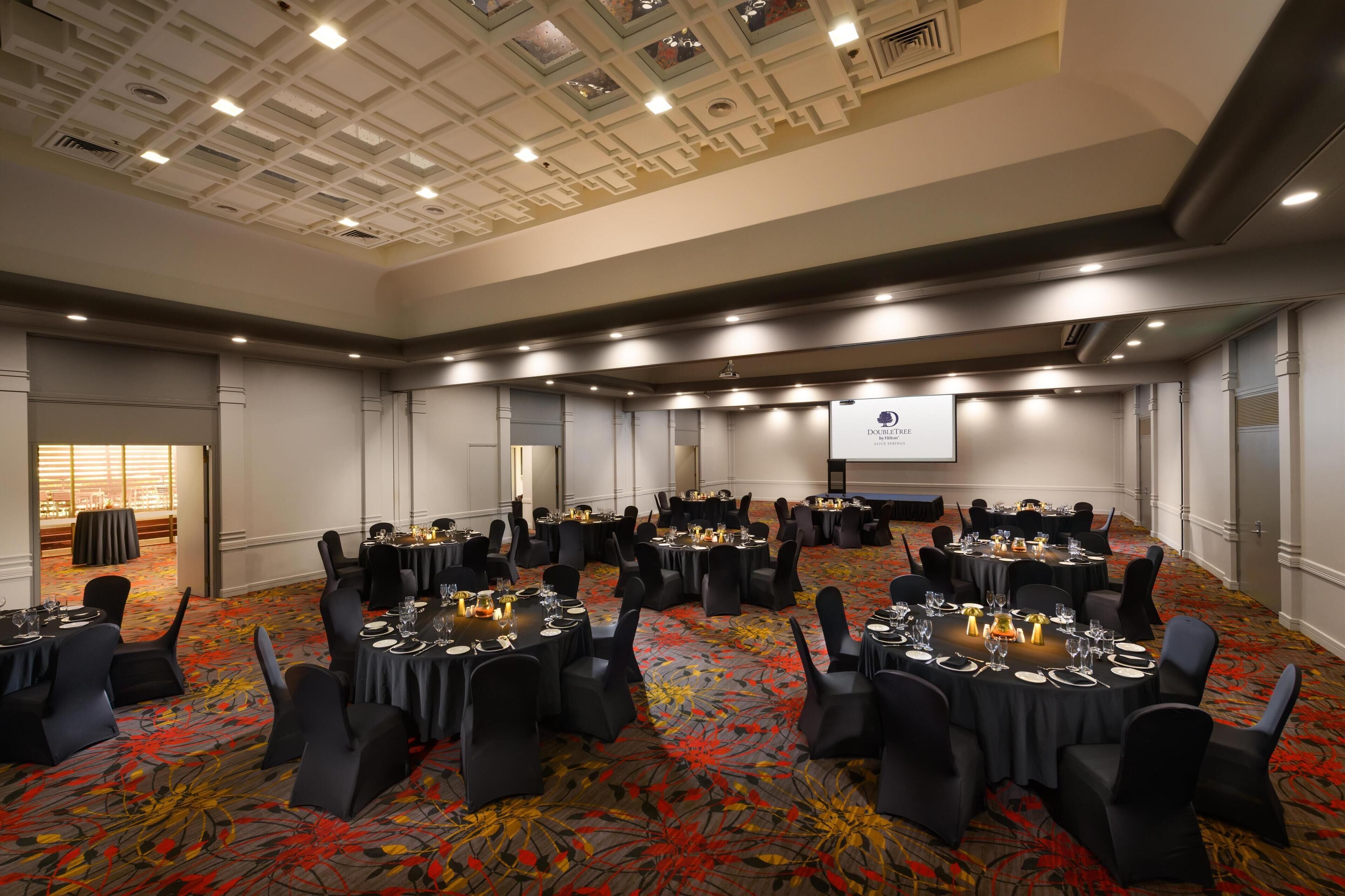 A conference room with round tables, black chairs, and a projector screen.