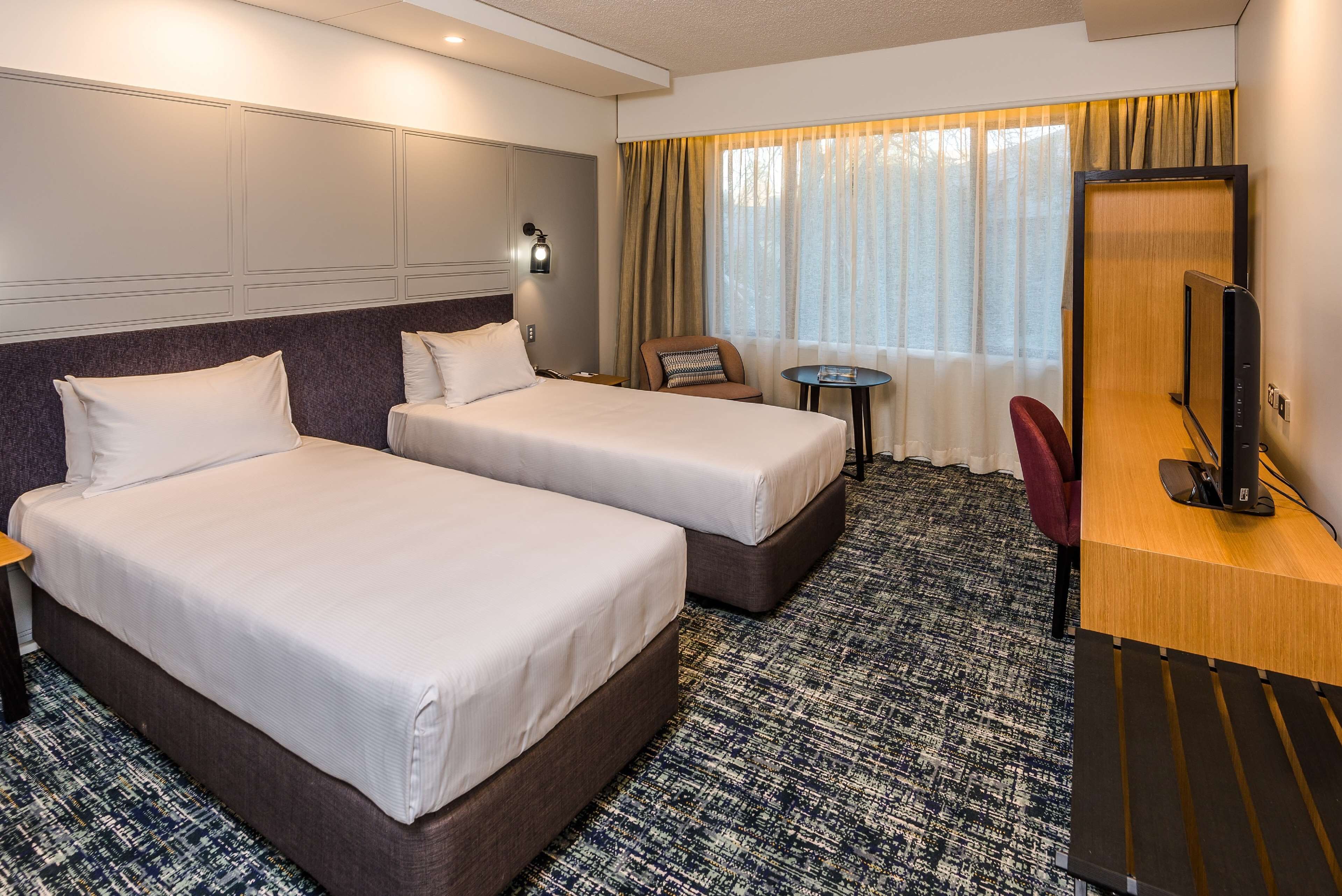 Habitación de hotel con dos camas, un escritorio con computadora, una silla y una mesita.