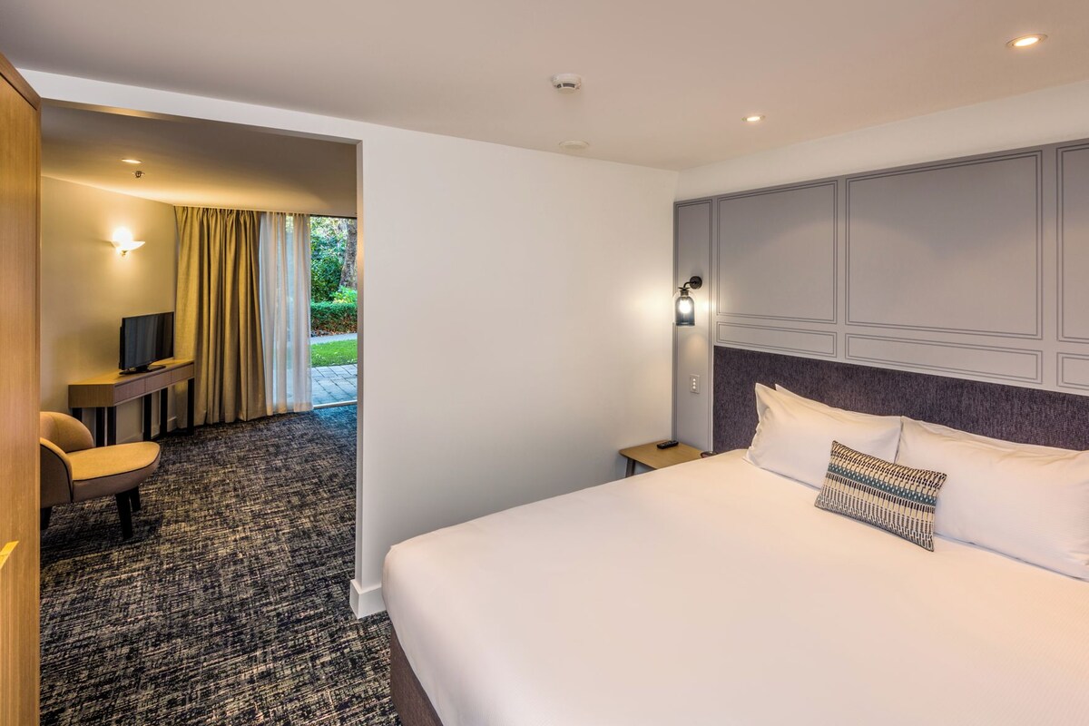 A hotel room with a bed, a desk, a chair, and a television.