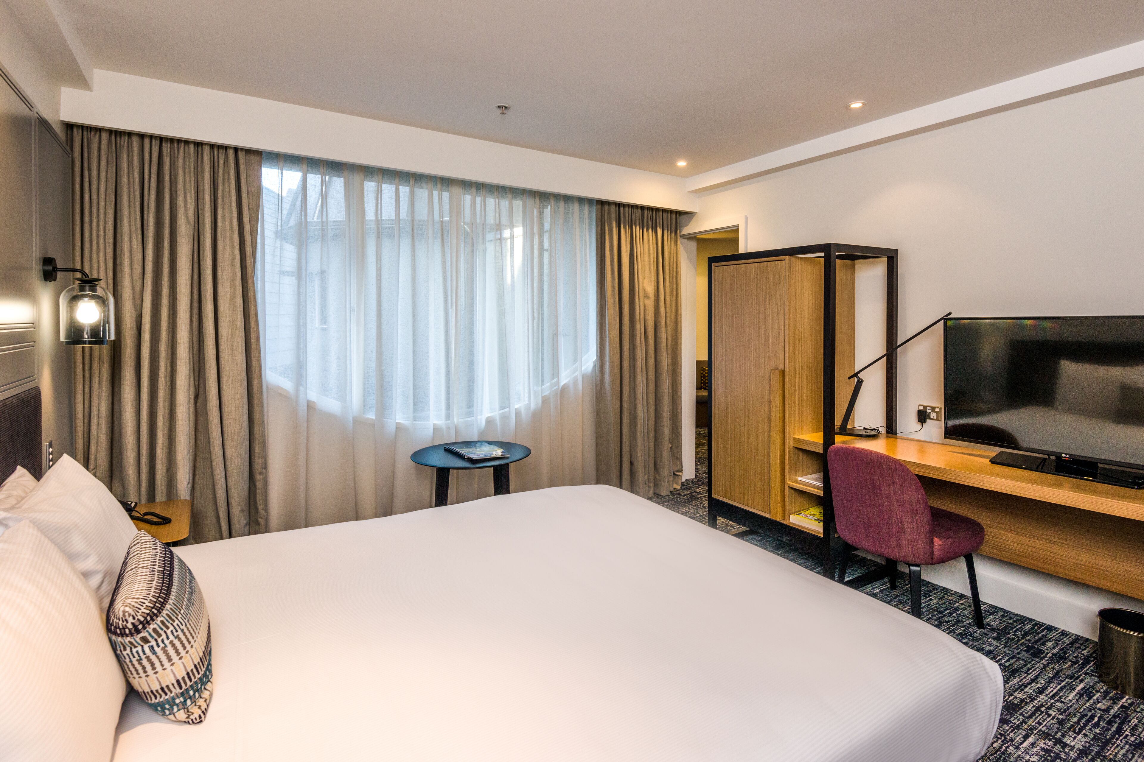 Habitación de hotel con una cama grande, un escritorio con una silla, un televisor y una mesita.