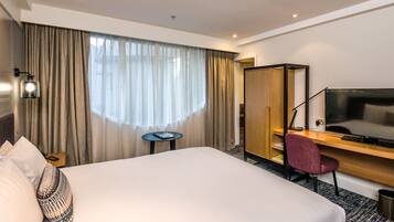 Habitación de hotel con una cama grande, un escritorio con una silla, un televisor y una mesita.