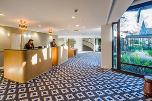 A reception area with a wooden reception desk, a receptionist, and a guest service area. - Chateau on the Park - Christchurch, a DoubleTree by Hilton (Christchurch)