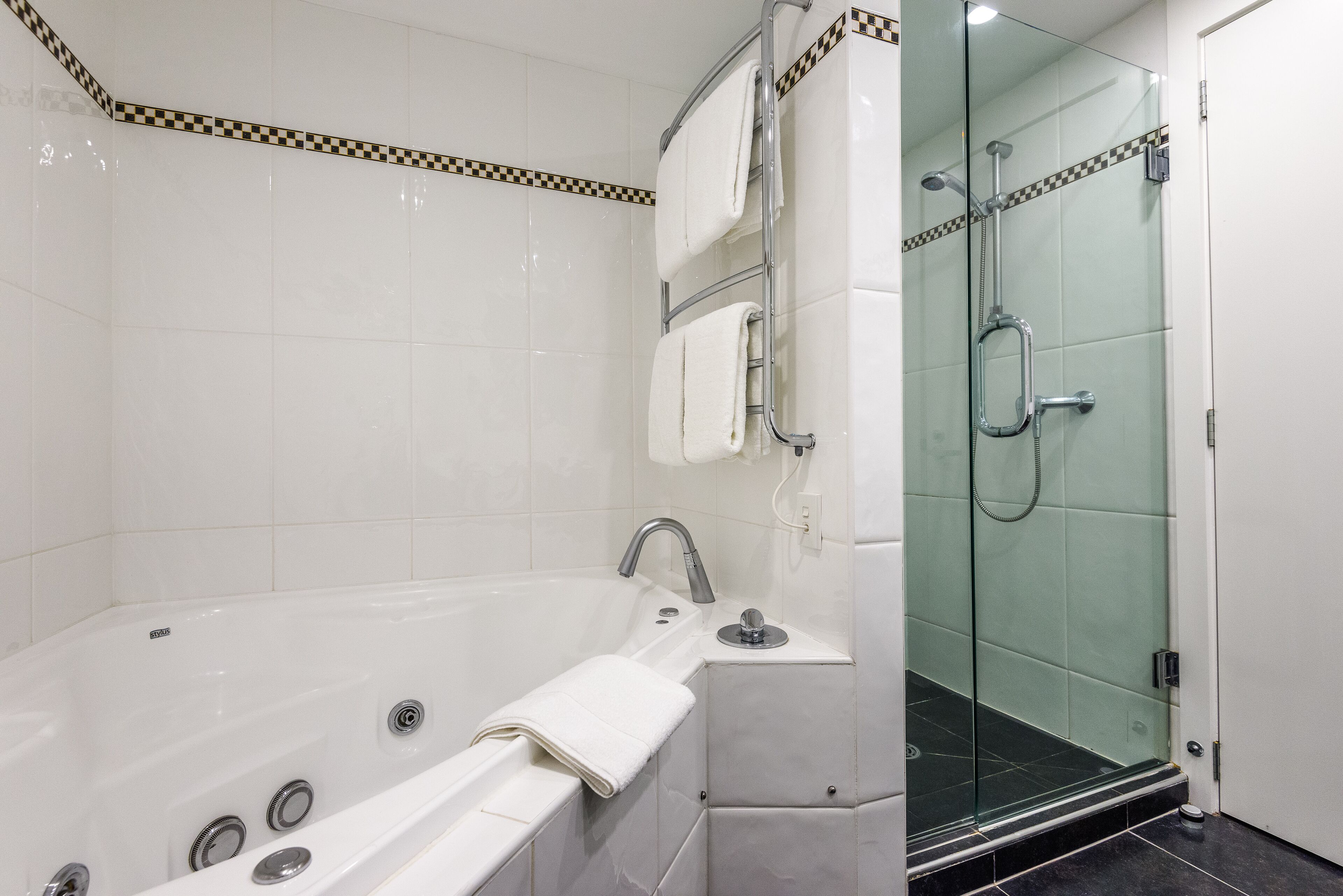A modern bathroom with a glass-enclosed shower, a separate bathtub with a built-in seat, and a vanity with a mirror and towel rack.