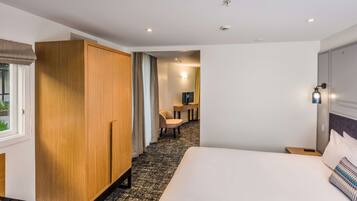 A hotel room with a large bed, a wooden wardrobe, a desk with a chair, and a small table.