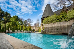 A swimming pool with lounge chairs, surrounded by trees and a bamboo fence. - Chateau on the Park - Christchurch, a DoubleTree by Hilton (Christchurch)