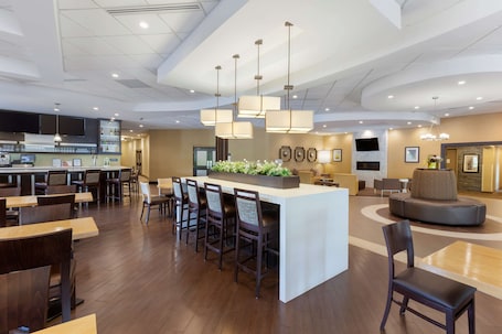A modern hotel lobby with a central bar area, seating arrangements, and a fireplace.