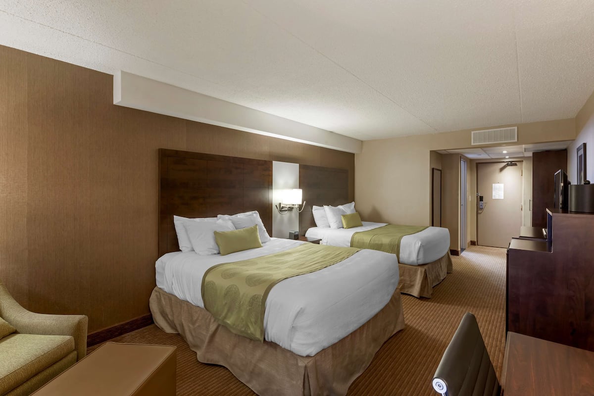 A hotel room with two beds, a desk, a chair, and a minibar.