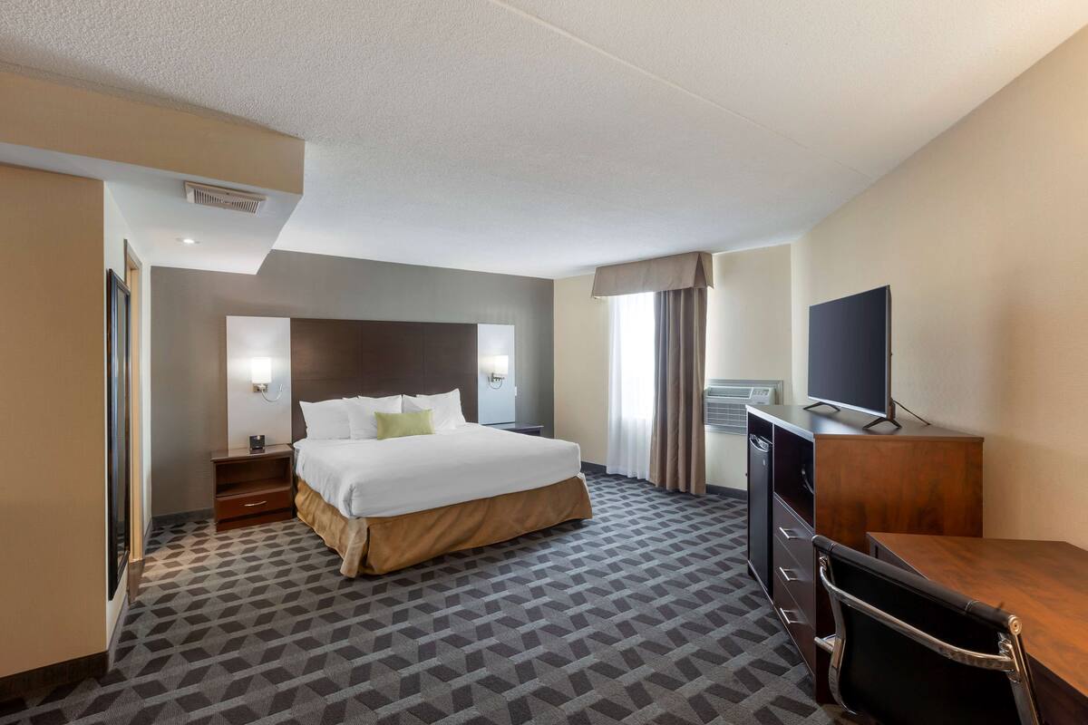 A hotel room with a large bed, a desk, a television, and a window with curtains.