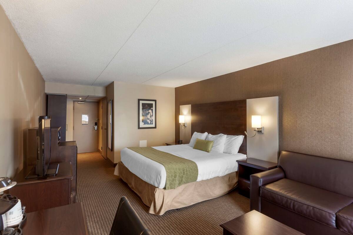A hotel room with a large bed, a sofa, a desk, and a television.