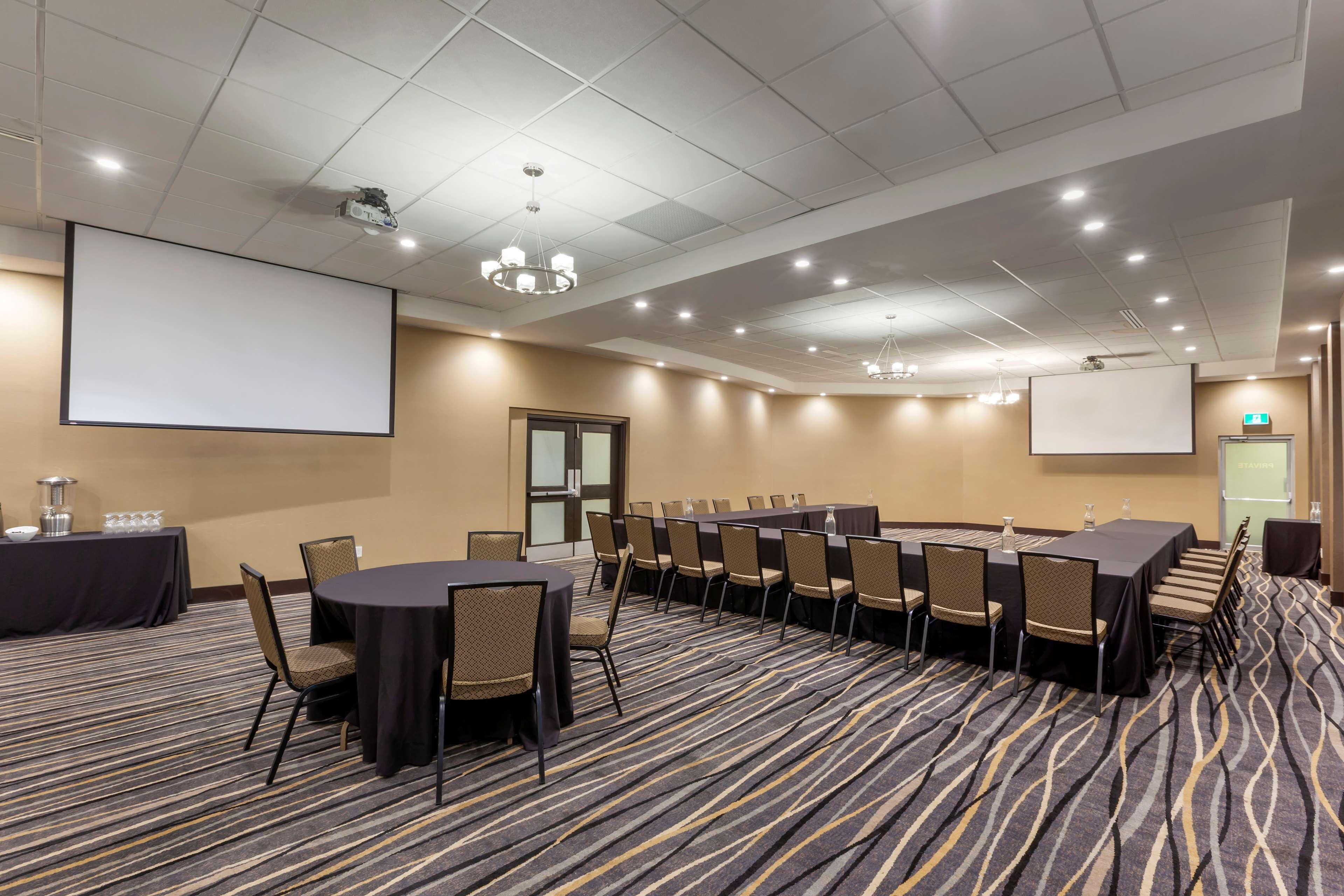 A conference room with a large screen, multiple tables, and chairs arranged for meetings.