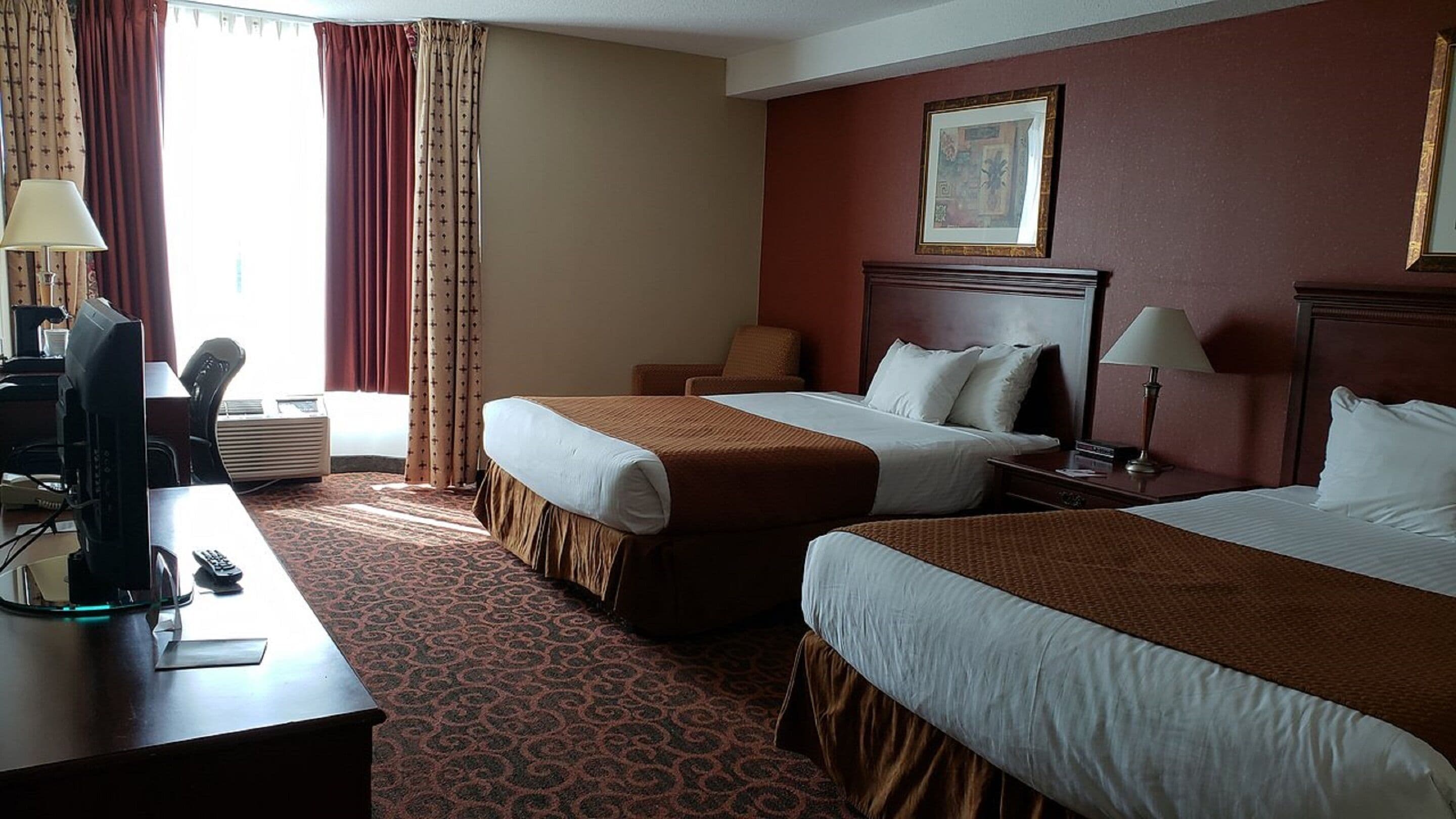 A hotel room with two beds, a desk with a computer, a chair, and a window with curtains.