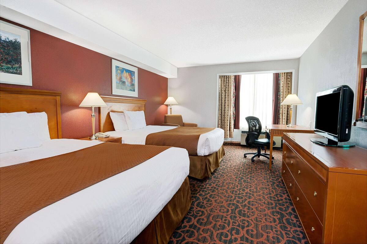 Habitación de hotel con dos camas, un escritorio, una silla, un televisor y un aparador.