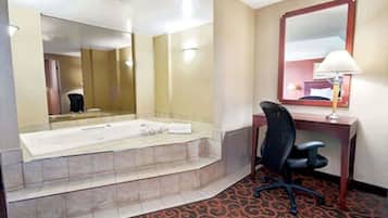 A hotel room with a large bathtub, a desk with a chair, and a mirror on the wall.