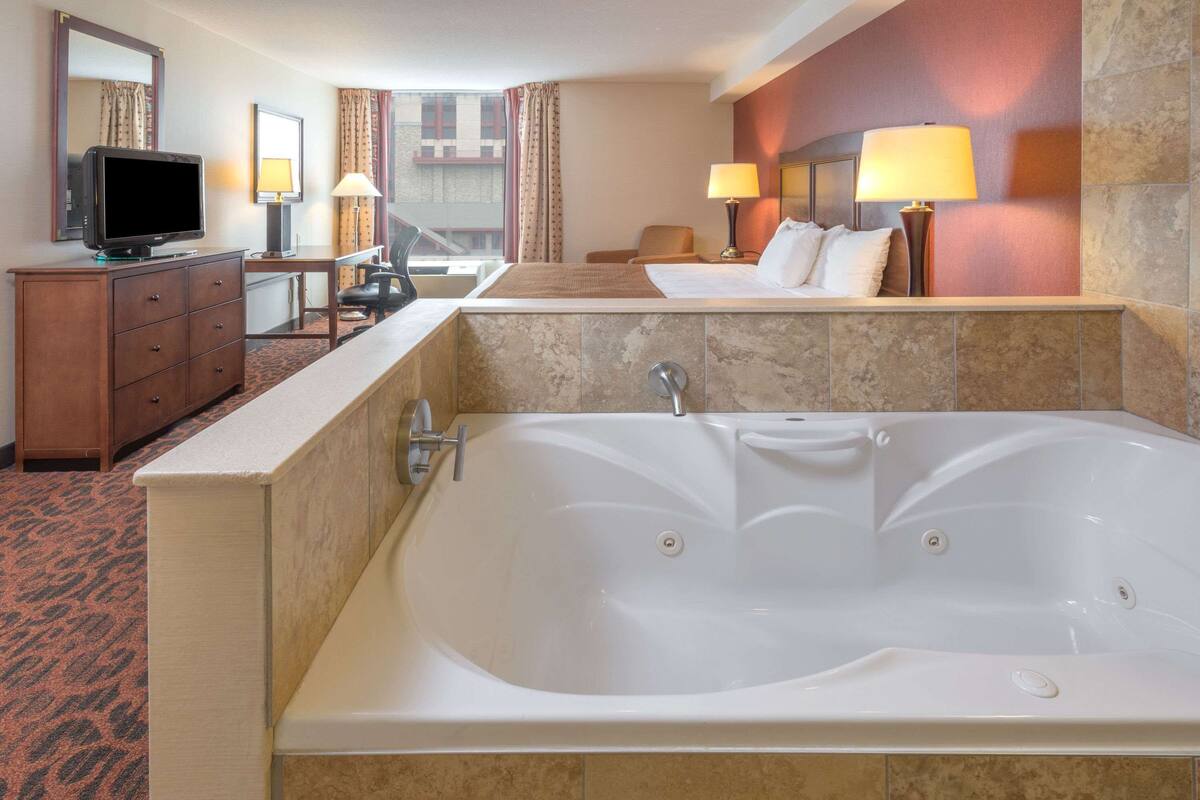 Habitación de hotel con una bañera grande, televisor, escritorio y cama.