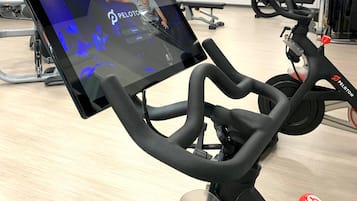 A stationary bike with a digital screen displaying a workout video, a mirror, and gym equipment in the background.