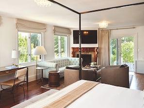 A spacious bedroom with a large bed, a sitting area with a sofa, a fireplace, and a television mounted on the wall.