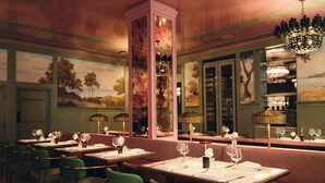 Interior de restaurante con sillas tapizadas de verde, mesas de madera y una araña.