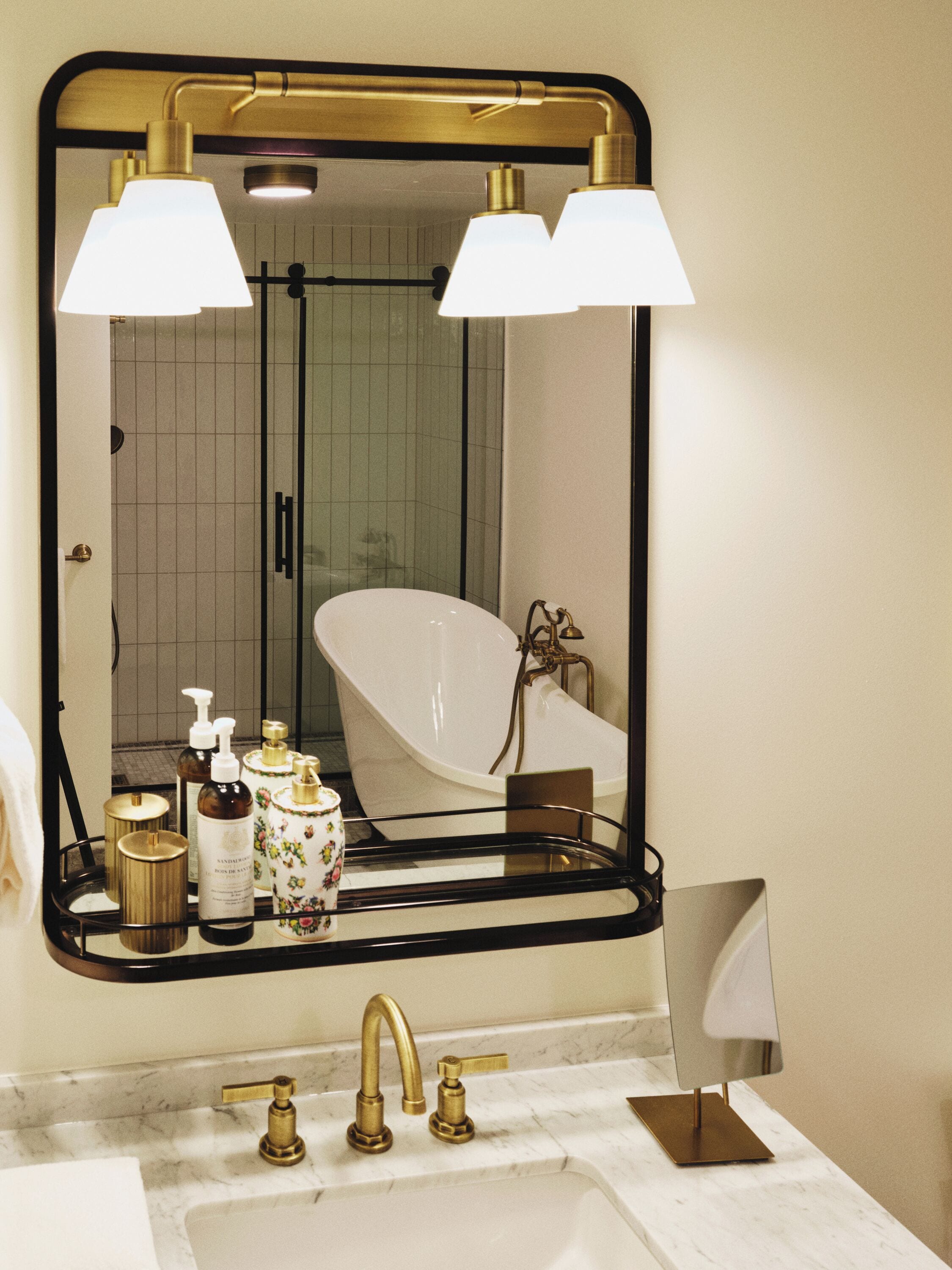 A bathroom with a large mirror, a bathtub, a sink with gold faucets, and a vanity with toiletries.