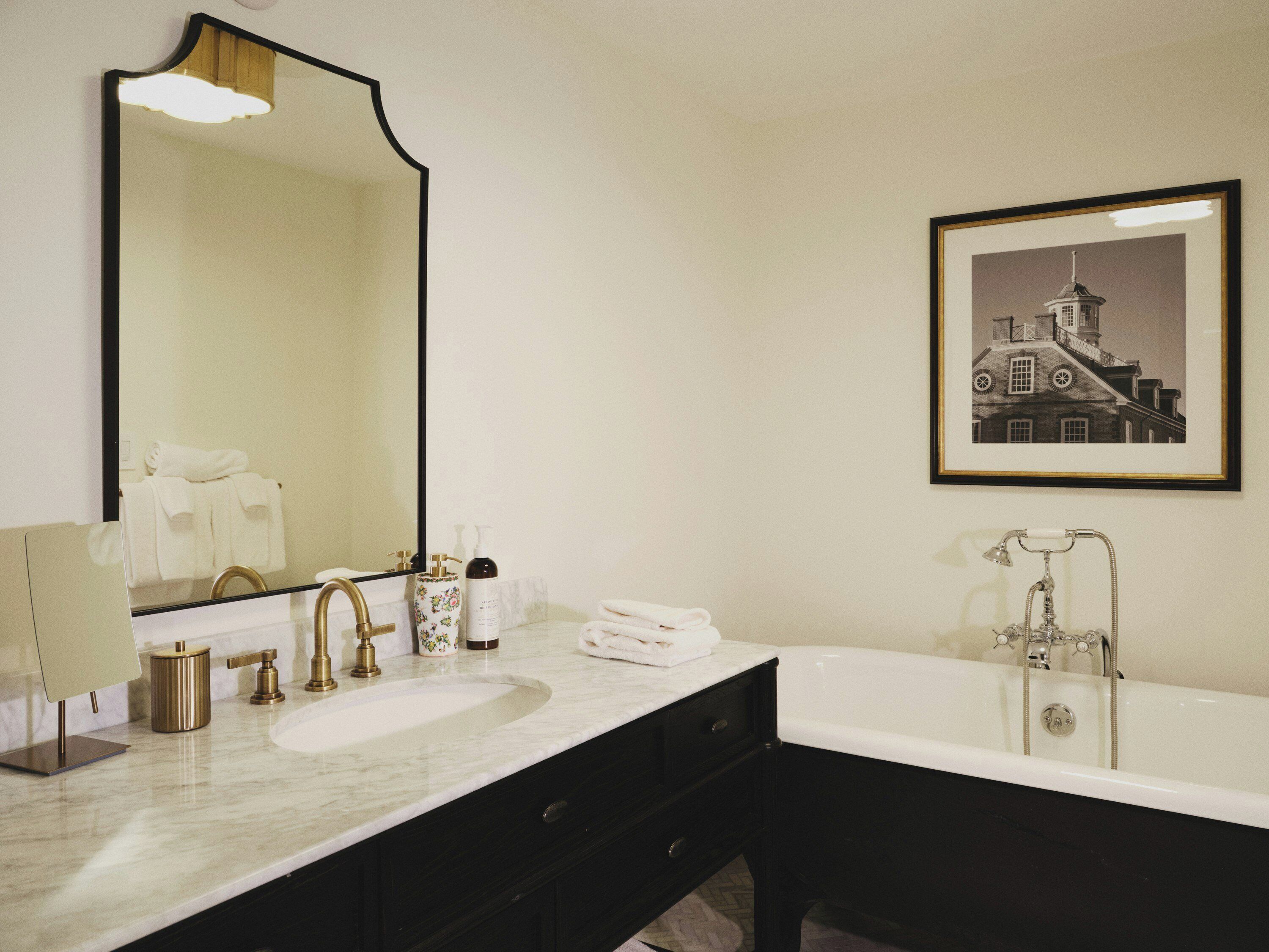 Une salle de bain avec un grand miroir, un lavabo, une baignoire et un tableau encadré au mur.