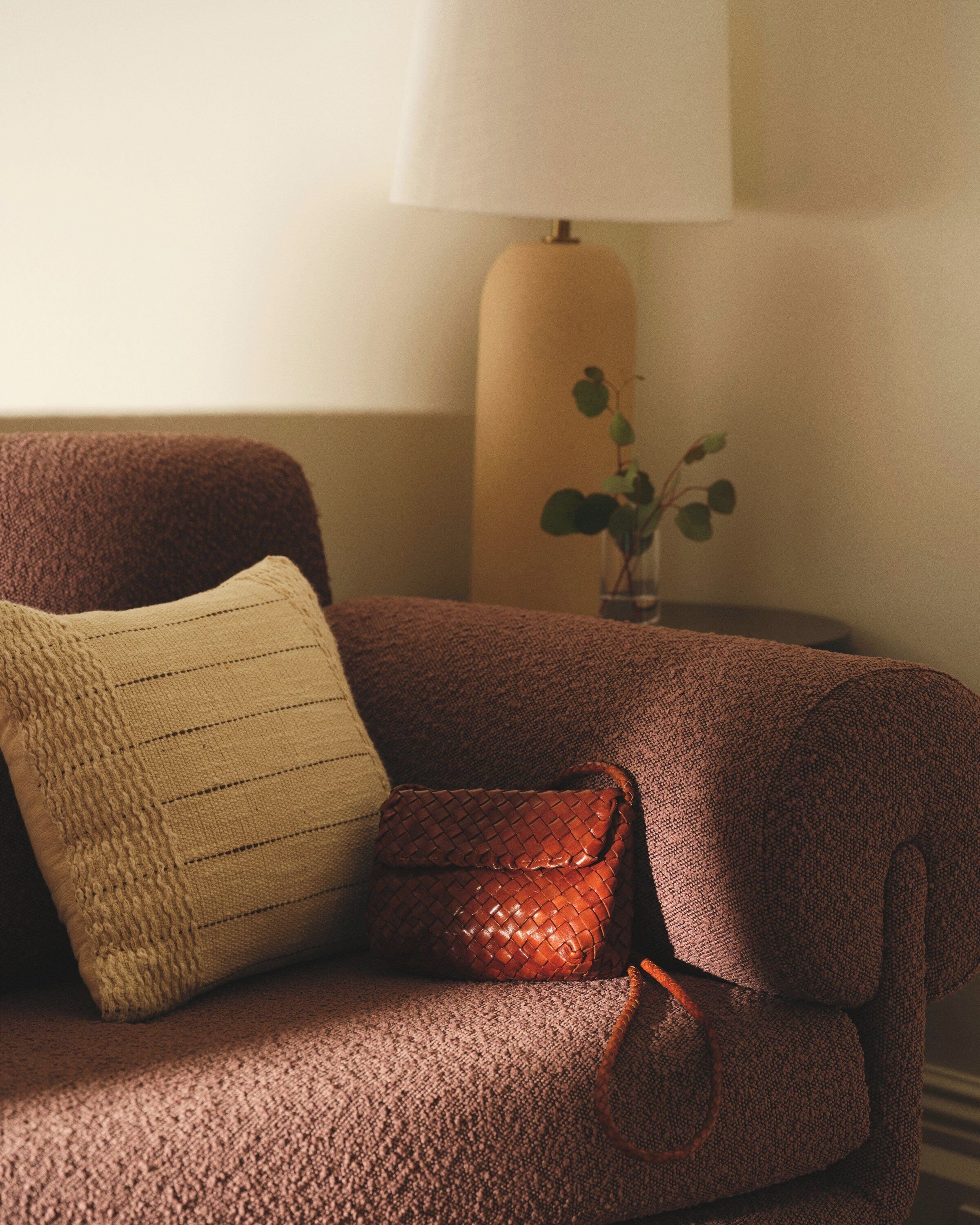 A brown sofa with a woven pillow and a leather bag.