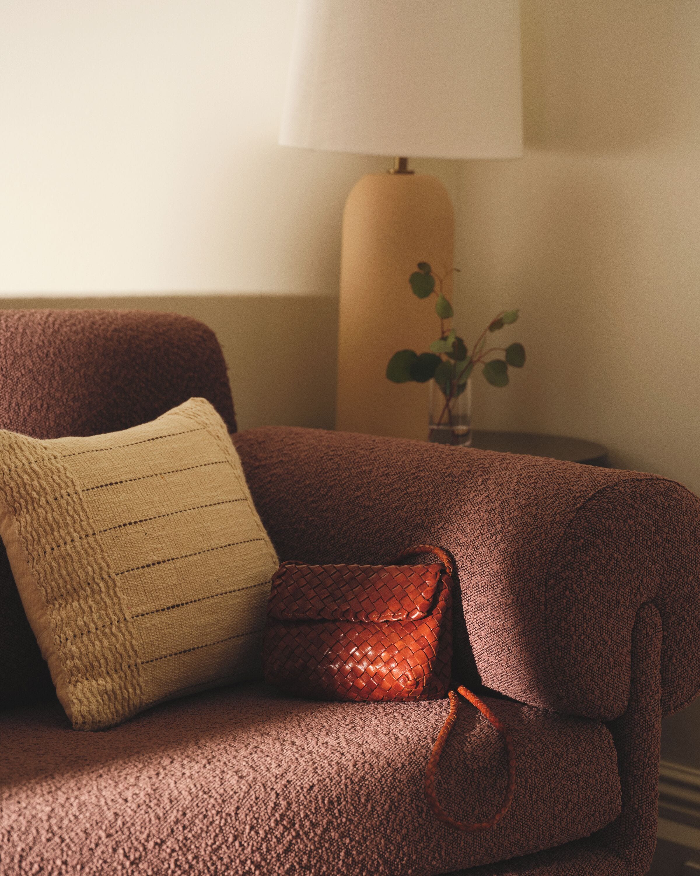 Un canapé recouvert d’un tissu texturé, un coussin et un petit sac en cuir marron.