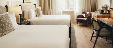 A hotel room with two beds, a desk, a chair, a lamp, and a window with curtains.