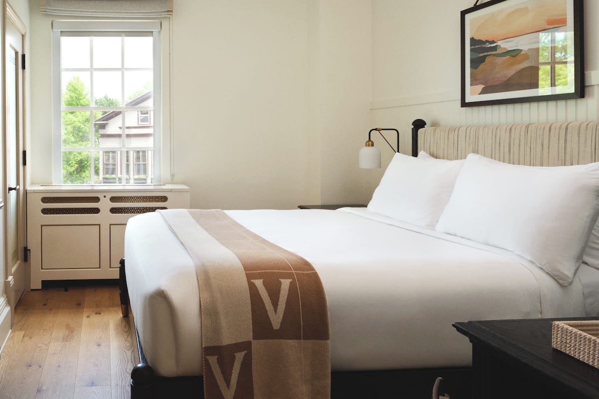 A neatly made bed with a V-patterned blanket, a bedside lamp, and a framed picture on the wall.