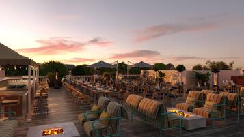 An outdoor dining area with multiple tables and chairs, a bar area, and a fire feature.