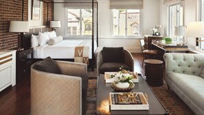 Habitación de hotel con cama con dosel, zona de estar con sofá y sillones, mesa de comedor y cocina.